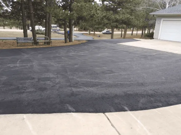 A wide residential driveway freshly paved in smooth black asphalt beside a concrete apron and garage